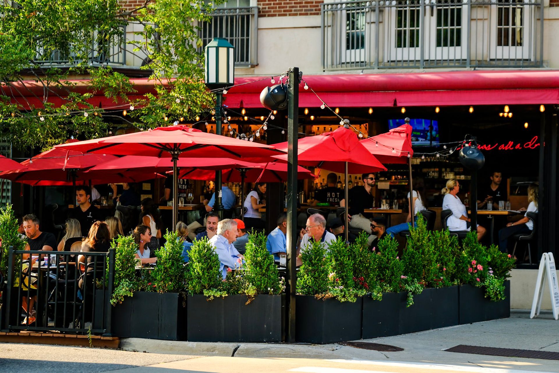 Diners relaxing on the patio at Townhouse Birmingham in downtown Birmingham, MI, under red umbrellas and string lights.