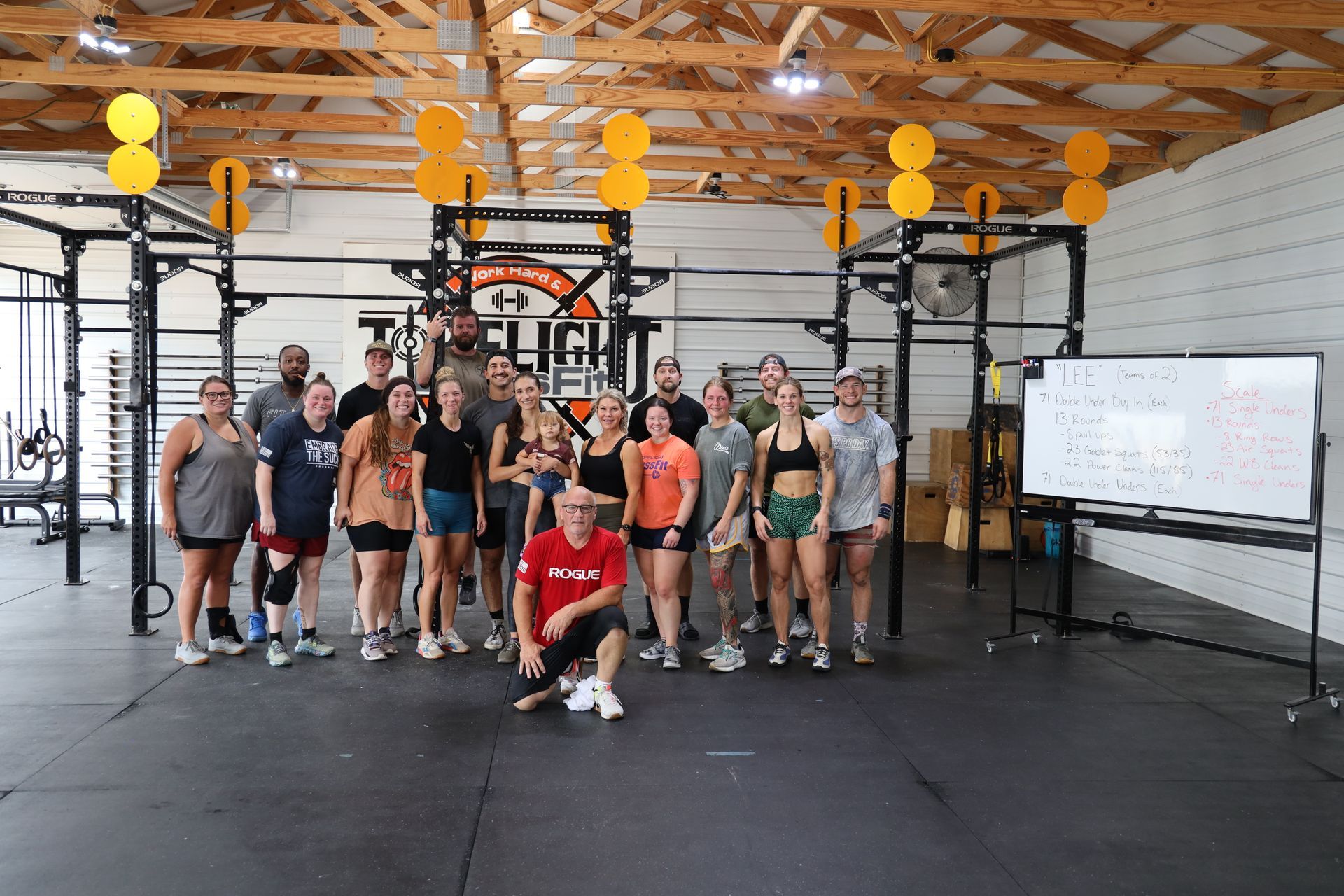 Group of people in gym posing. Some wearing athletic clothes. Man kneeling, holding red shirt.