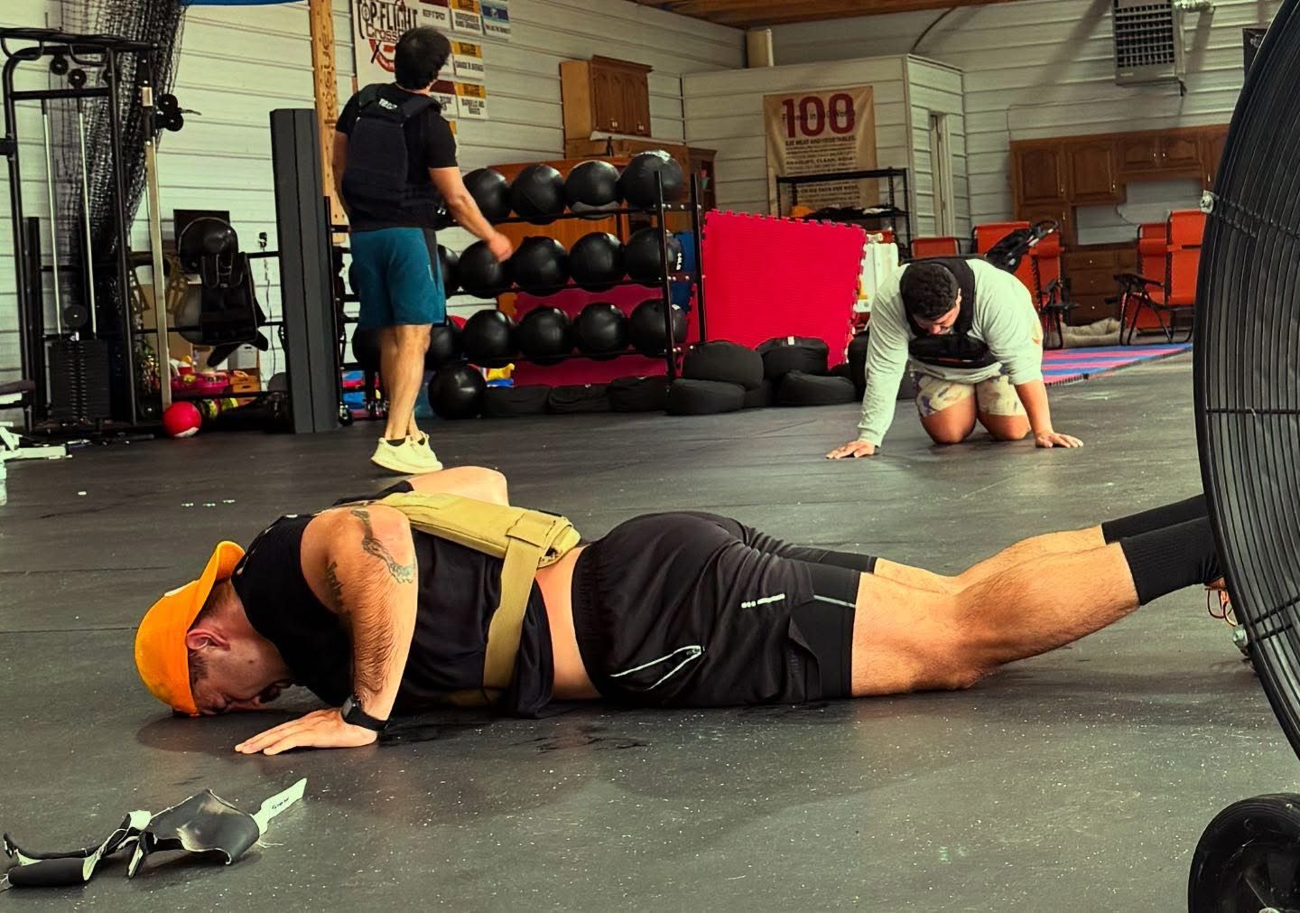 Man doing weighted push-ups in gym, others in background.