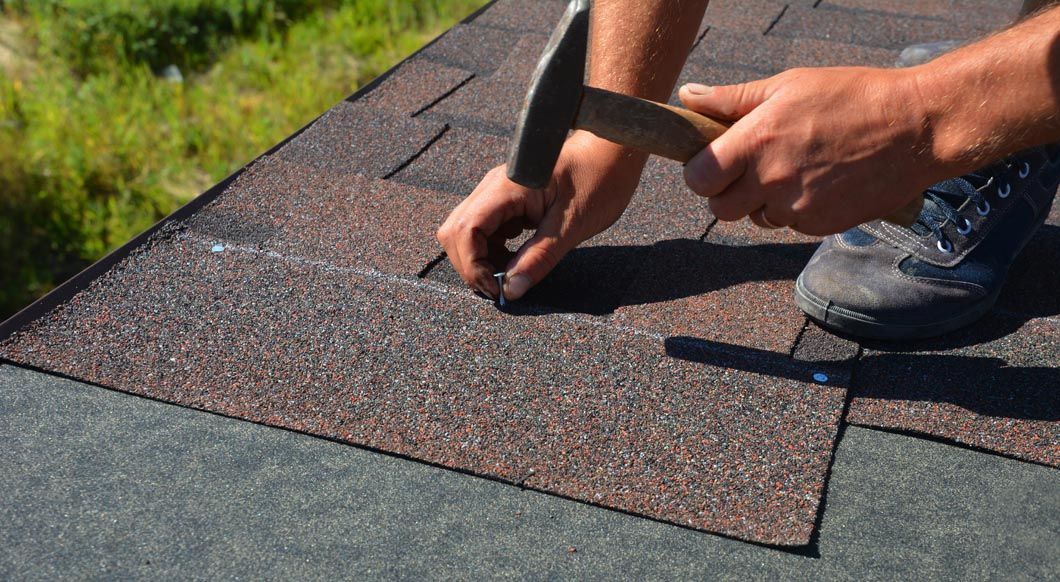 A man is hammering nails into a roof with a hammer.