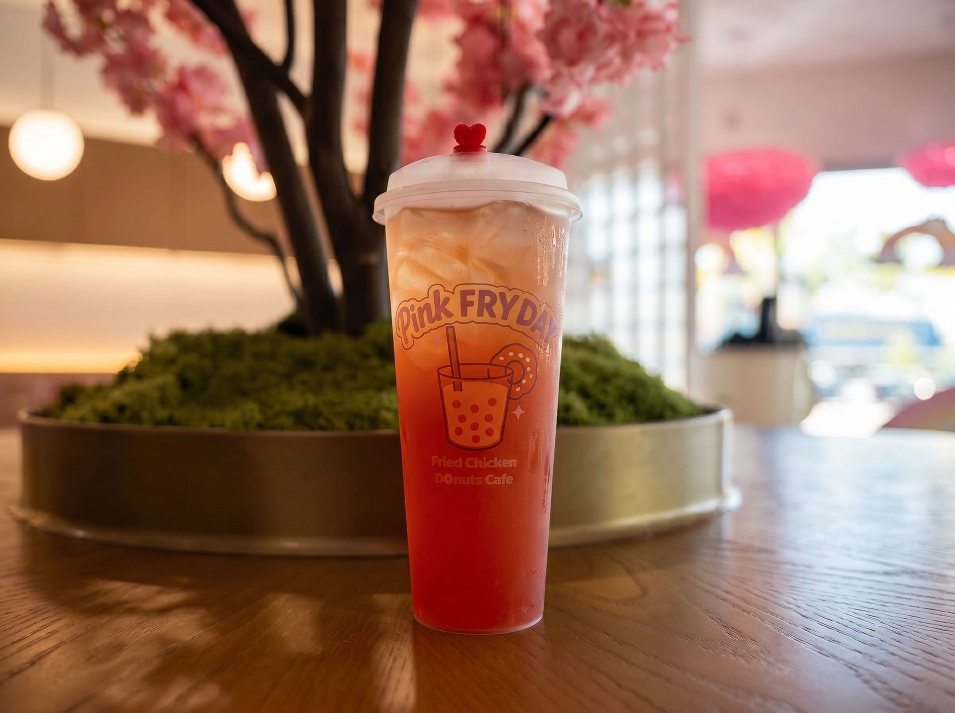 Pink drink with whipped cream in a clear cup on a wooden table, with pink blossoms in the background