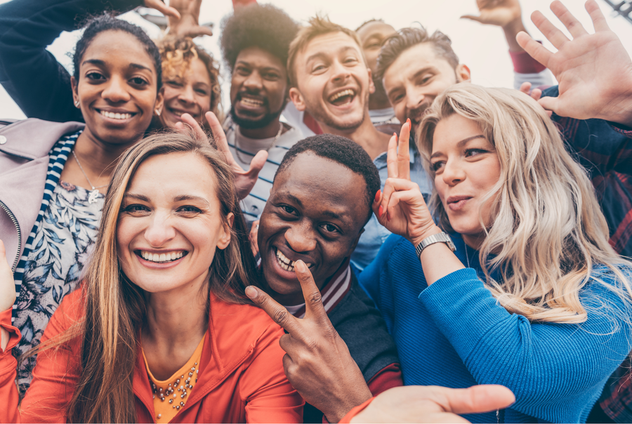 Group of diverse friends smiling and taking a selfie outside.
