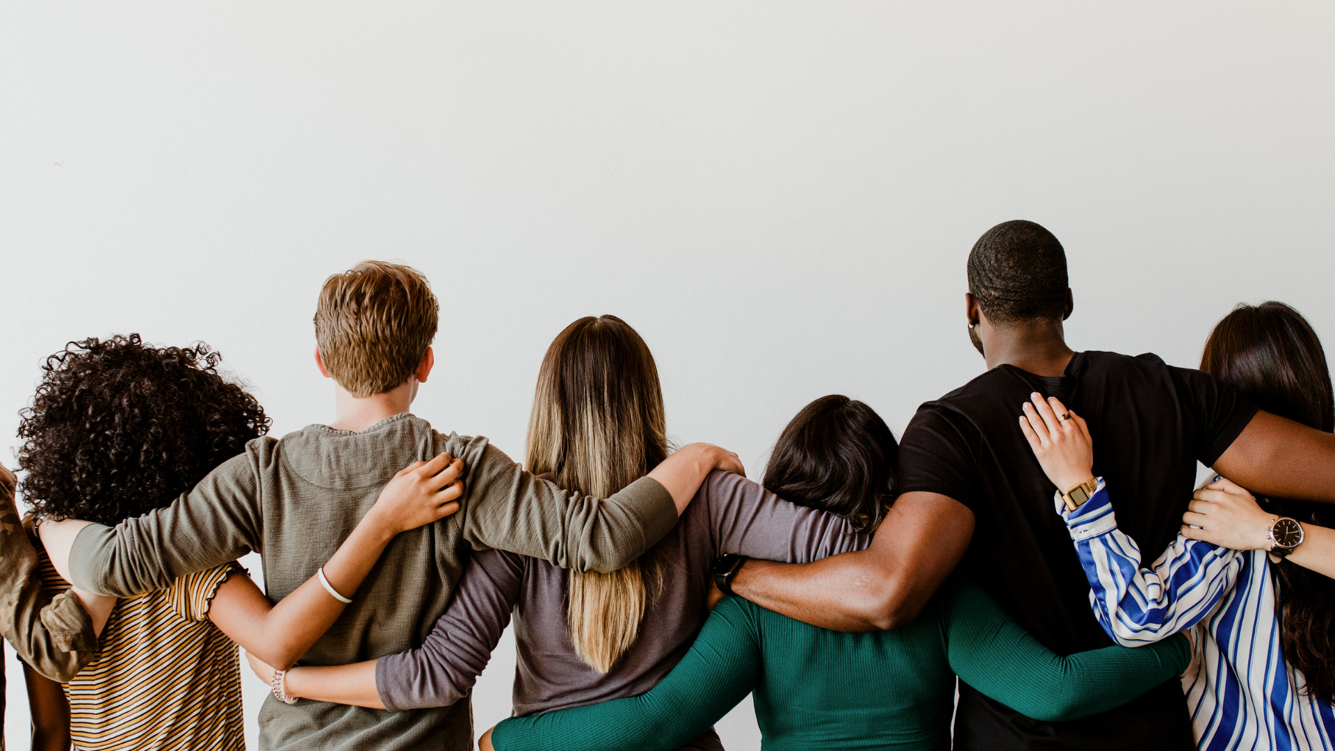 Woman with short hair and glasses laughs, holding a blue mug on a couch near a window; tattoo on leg.