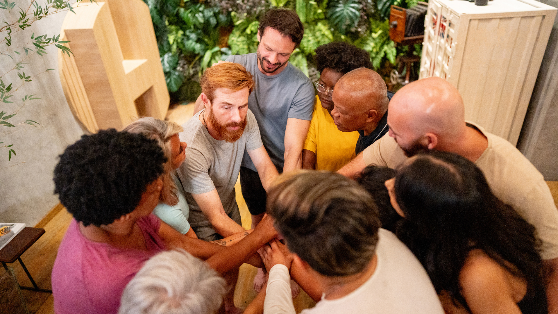 Group of diverse people with hands in a huddle, fostering teamwork and unity indoors.