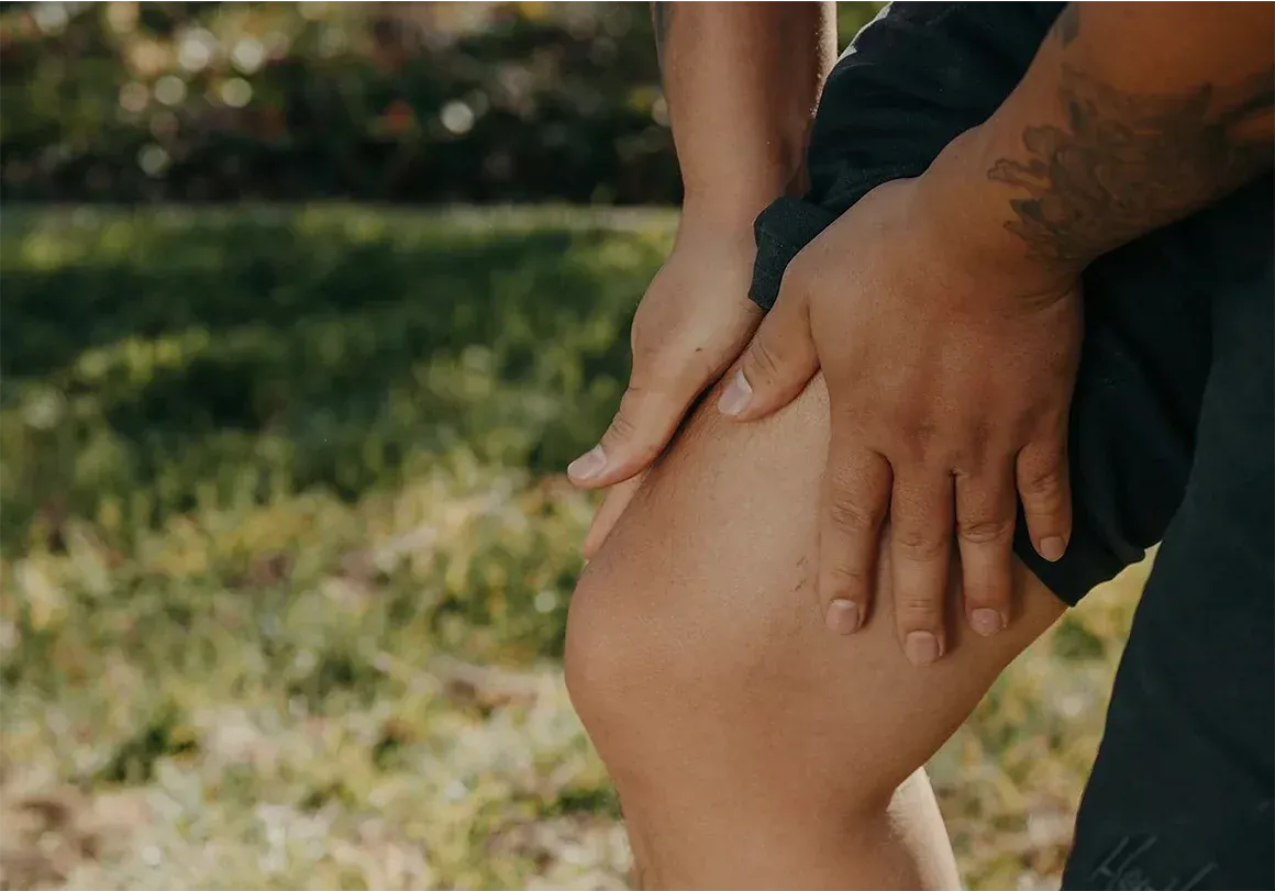 Person holding their knee, possibly in pain, outdoors on grass.