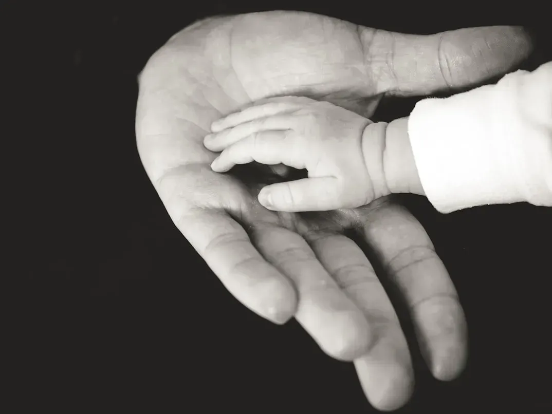 A baby holds a man 's hand in a black and white photo