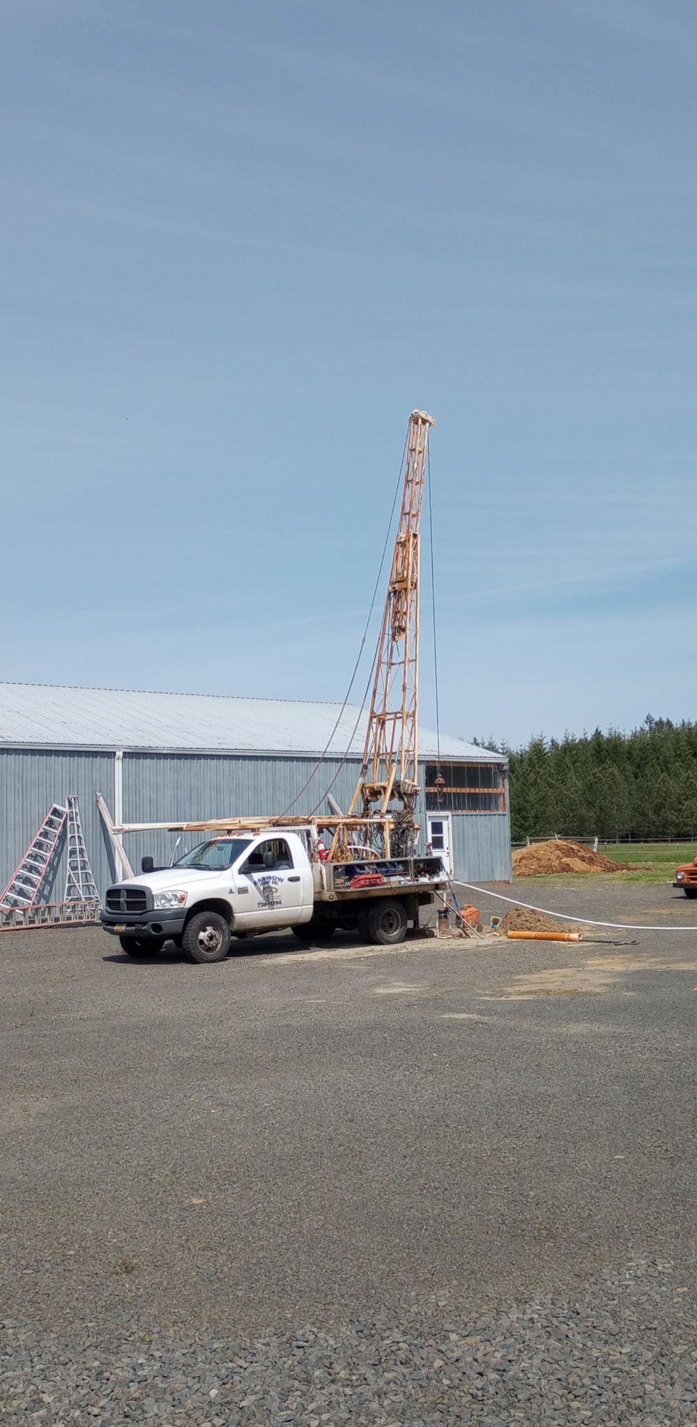 Blue well head and pipes with rusty metal components in a field with dry vegetation.