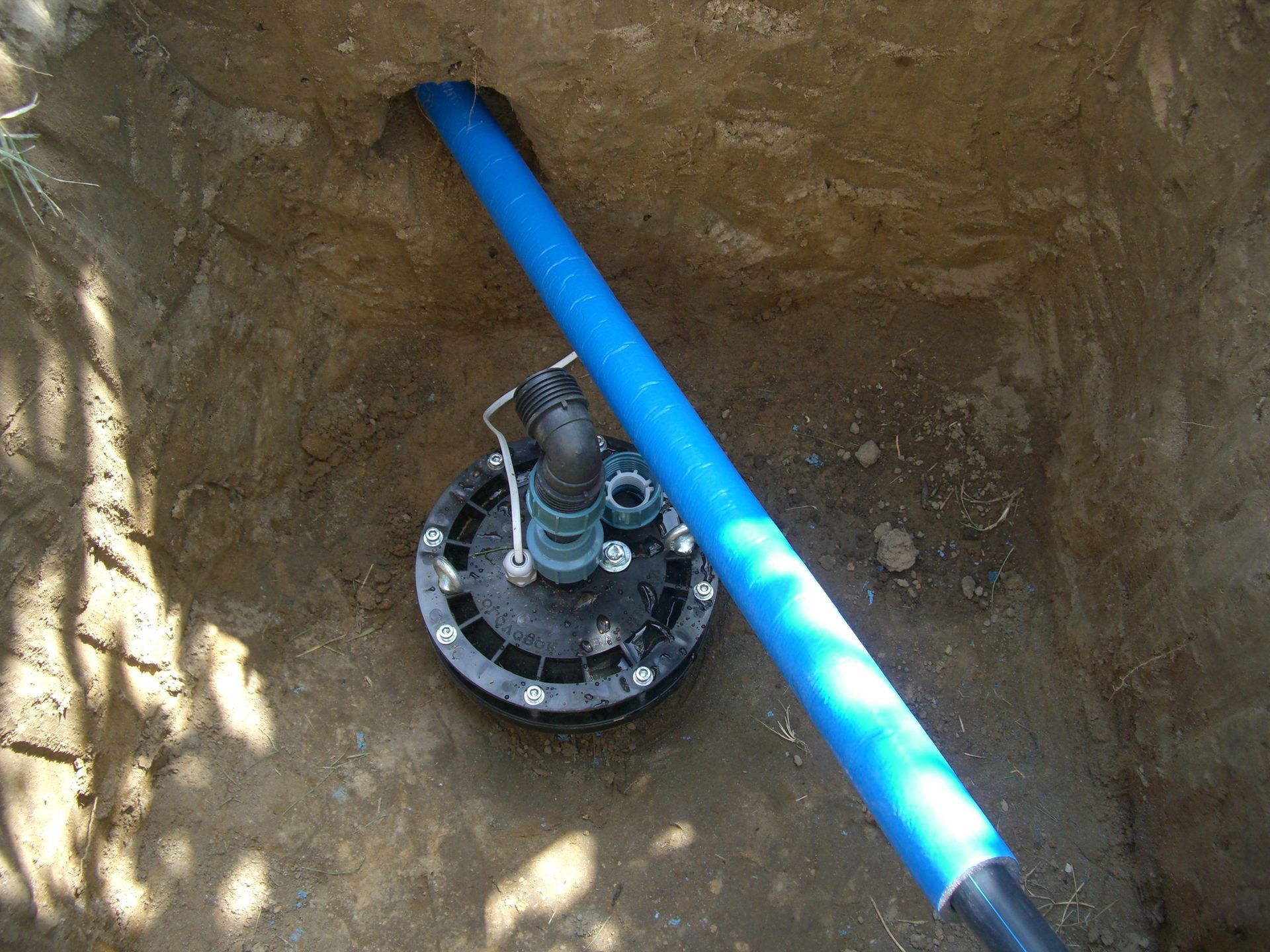 Well pump installation in dirt pit with blue and black pipes.