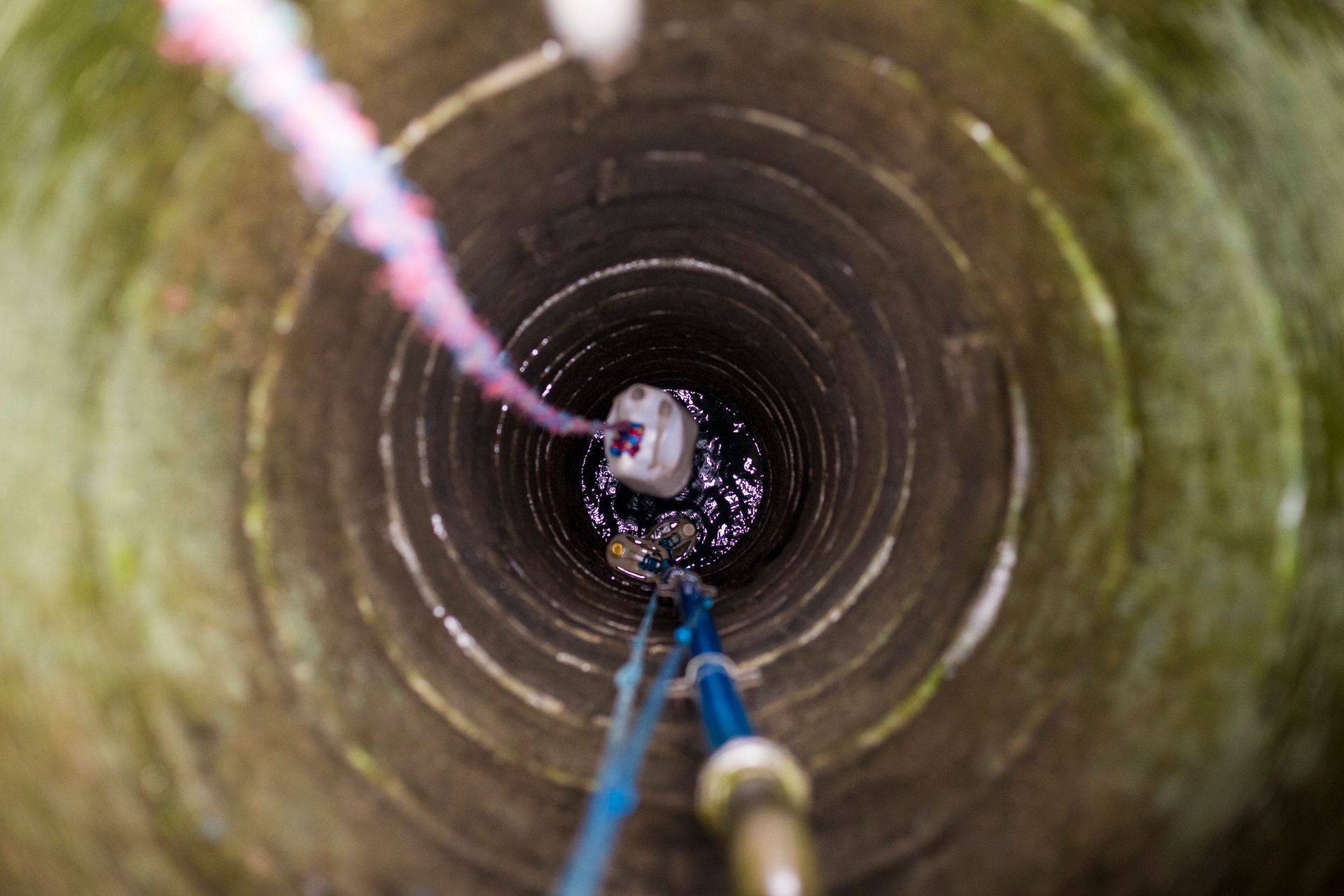 Looking down into a deep, circular well with ropes and a bucket visible inside.