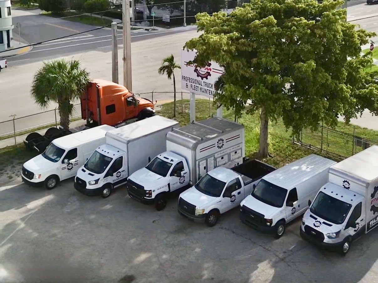Line of white service trucks parked next to each other, with an orange semi truck visible in the background.
