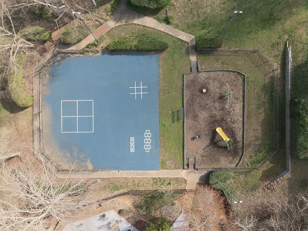 Aerial view of a playground with a blue court marked for games and a mulch area with a slide.