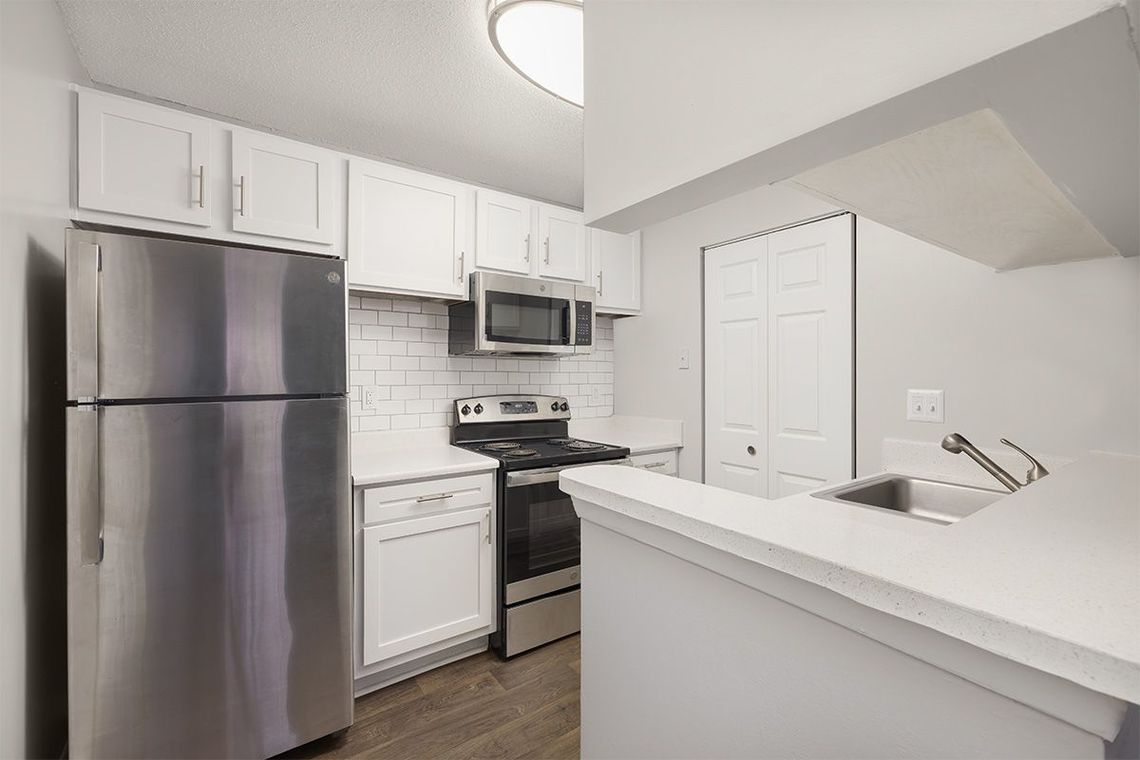 Bright kitchen with stainless steel appliances, white cabinets, and a white countertop.