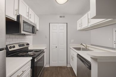A kitchen with white cabinets , a stove , a microwave , and a sink.