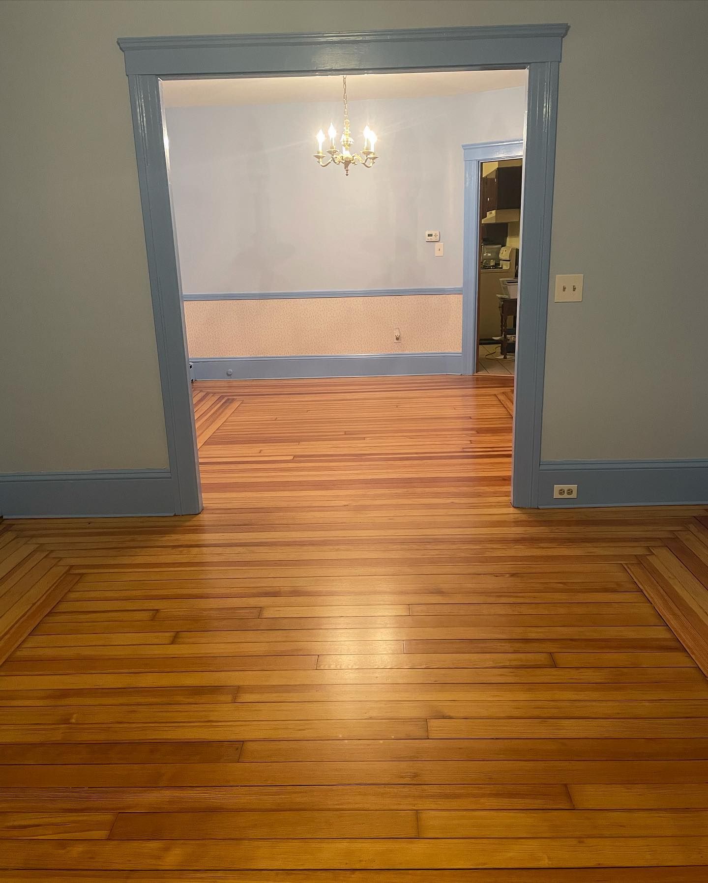 Hardwood floors lead into a room with blue walls, trim, and a chandelier.