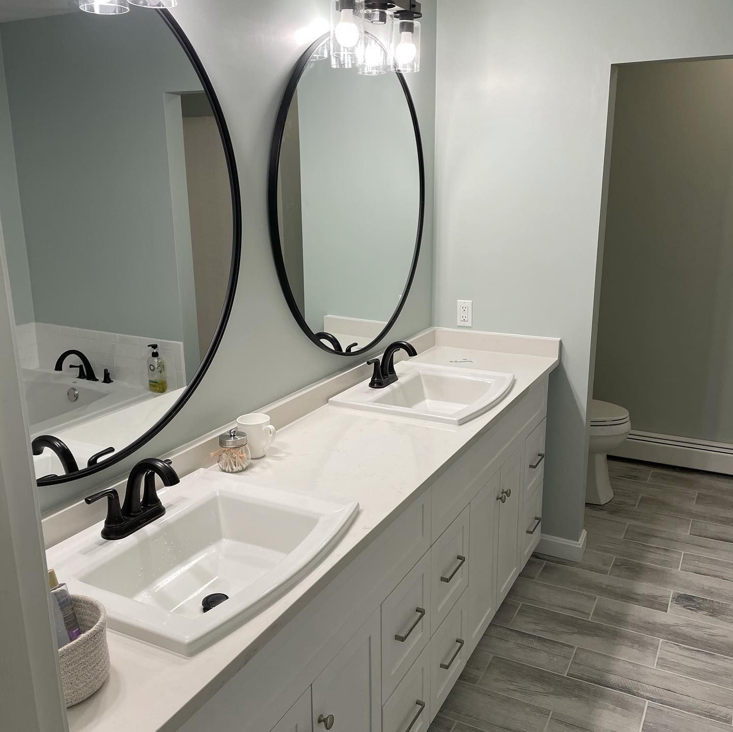 Bathroom with white double vanity, oval mirrors, black fixtures, and gray tile floor.
