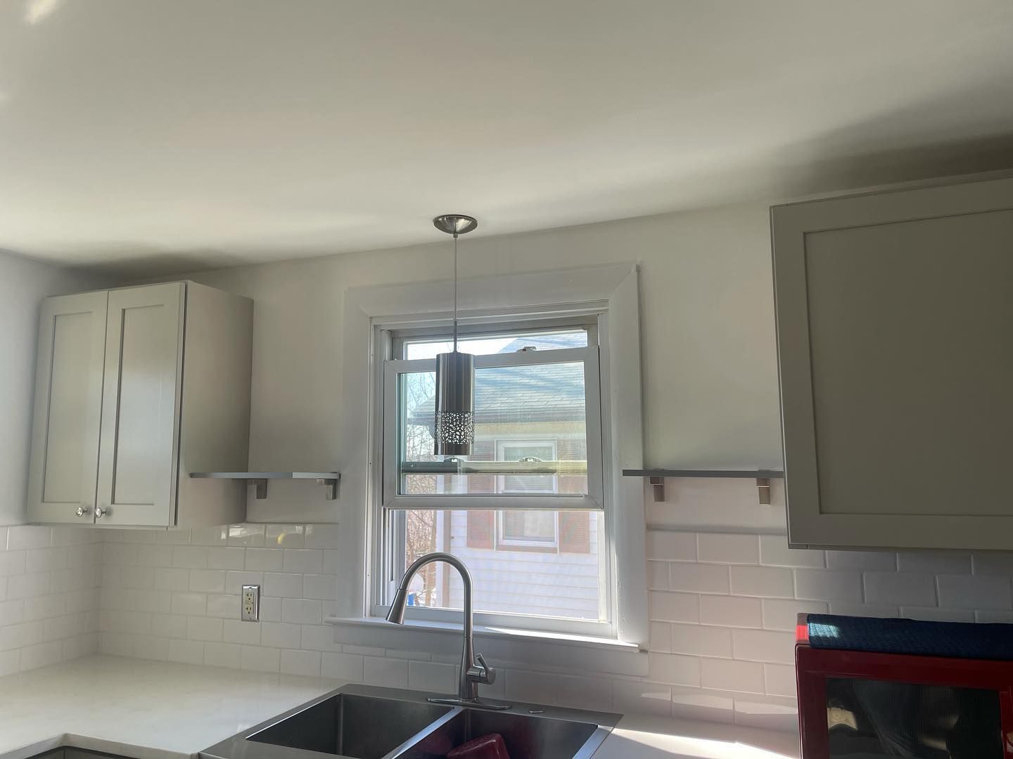 Kitchen with sink under a window, white cabinets, white tile backsplash, and a pendant light.