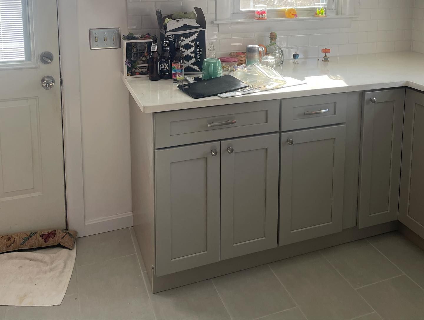 Gray kitchen cabinets with a white countertop and tile floor, next to a door.