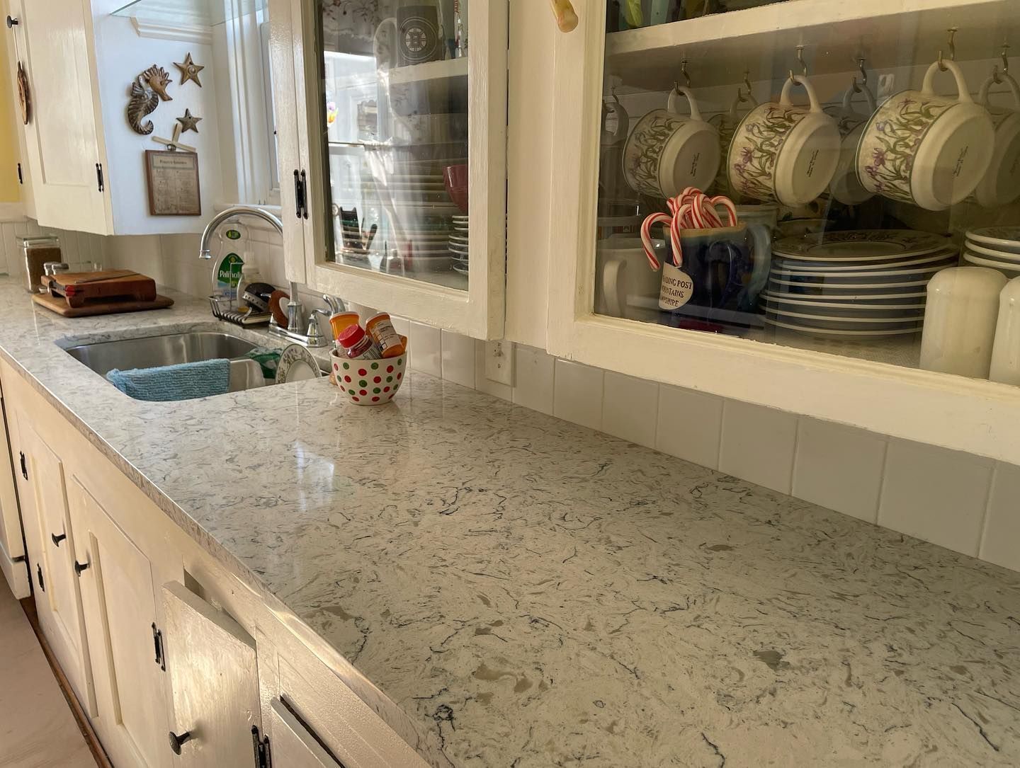 Kitchen countertop with sink and cabinets, dishes displayed, white and gray speckled surface.