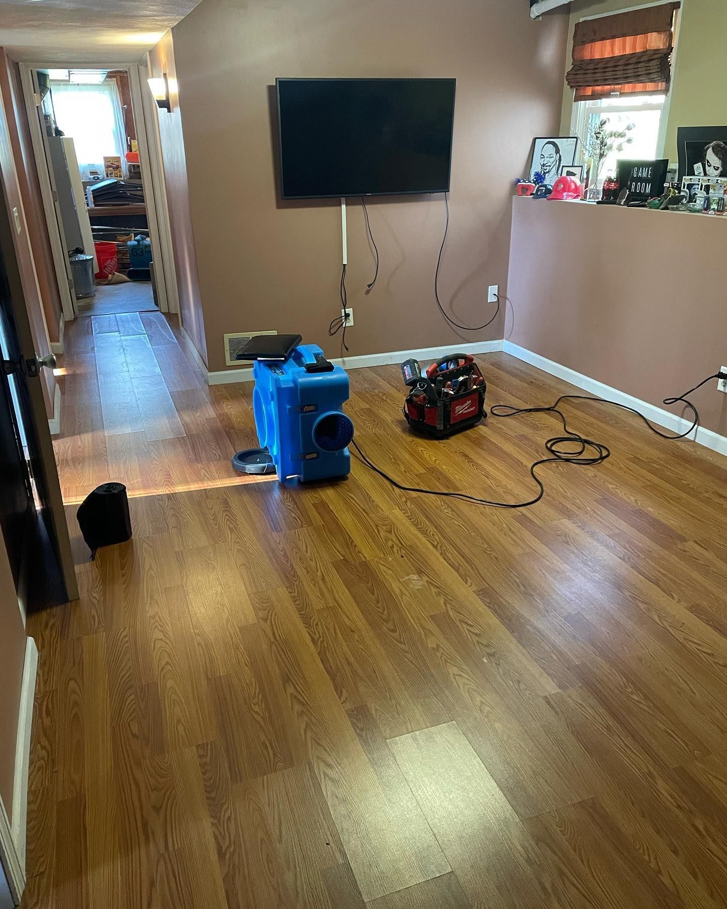 Room with a TV on wall, a blue and red air mover, and wood-like flooring.