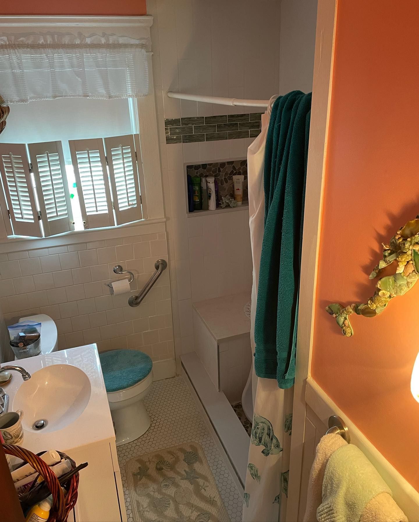 Small bathroom with a white sink, toilet, and bathtub. Coral walls and teal towels.