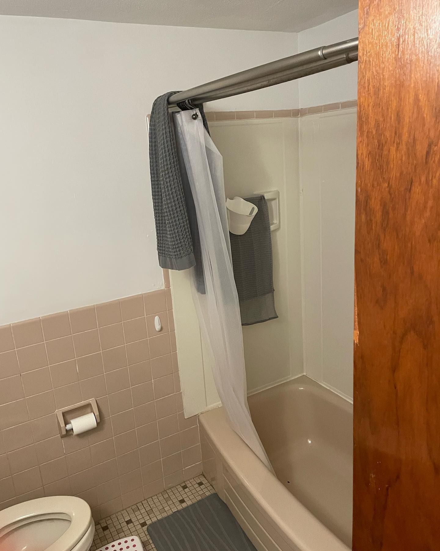 Bathroom with a pink-tiled wall, tub, shower curtain, and a towel.