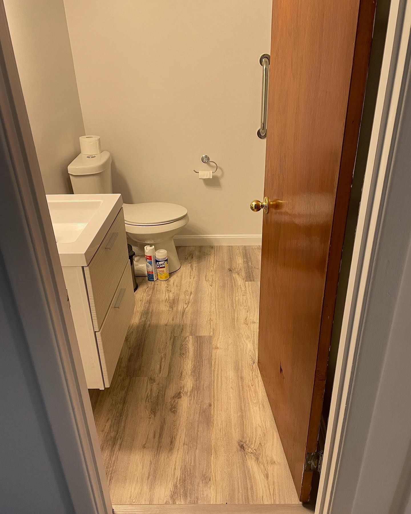 Bathroom interior with a toilet, sink, and partially open wooden door. Light gray flooring and white walls.