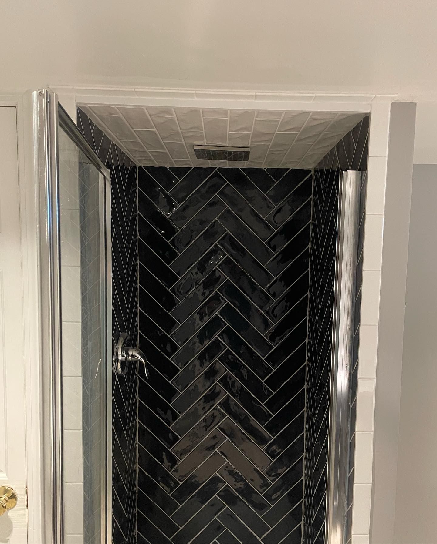 Shower stall with black herringbone tile, silver fixtures, and glass door.