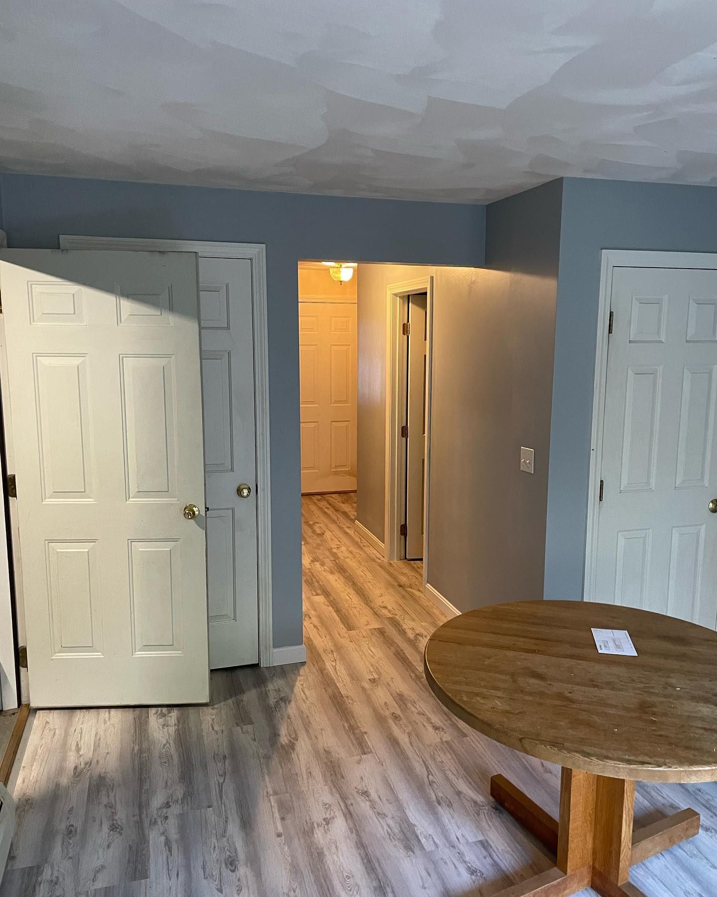 Hallway with white doors, light wood floor, round wooden table.