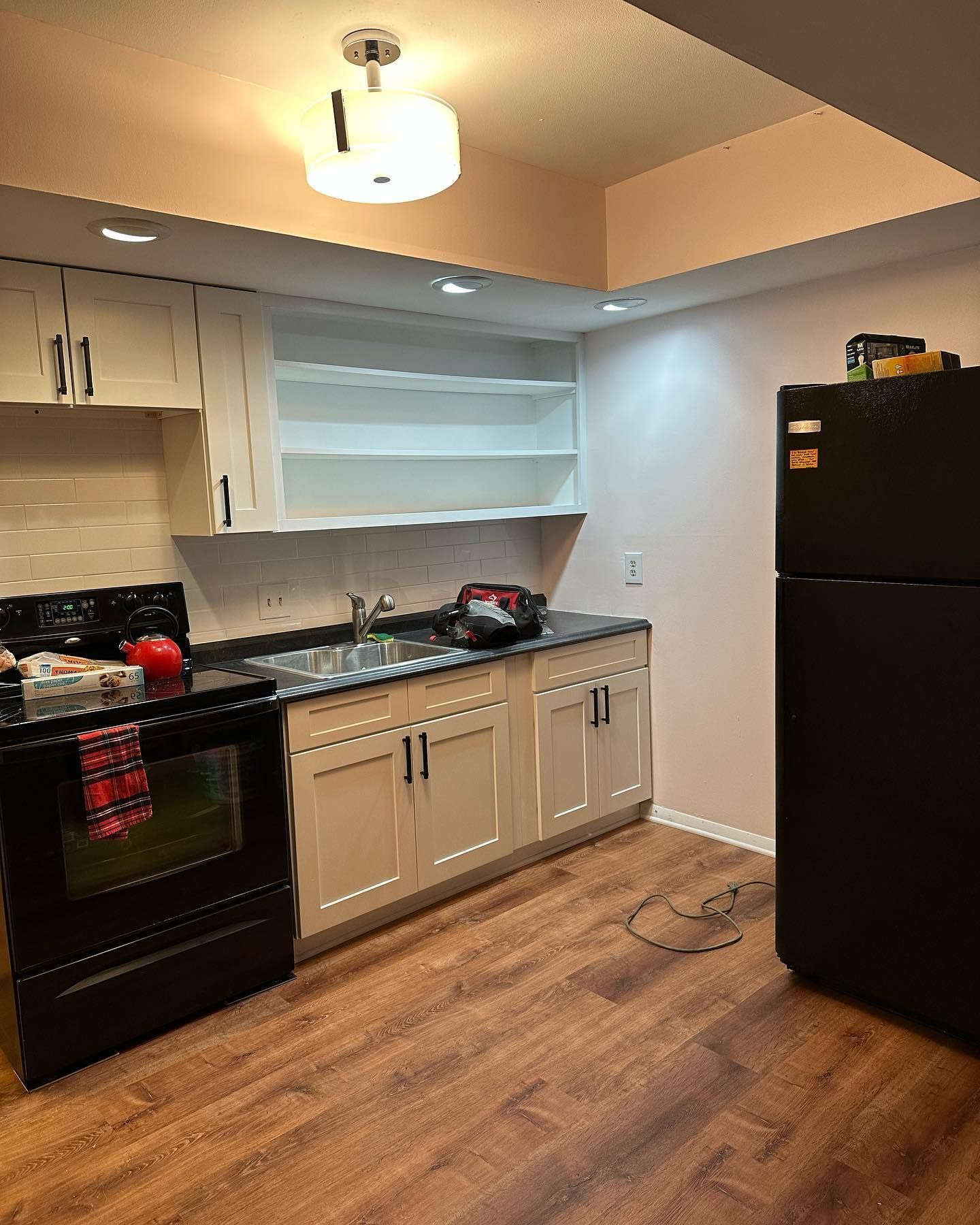 Kitchen with black appliances, white cabinets, and wood-look flooring.