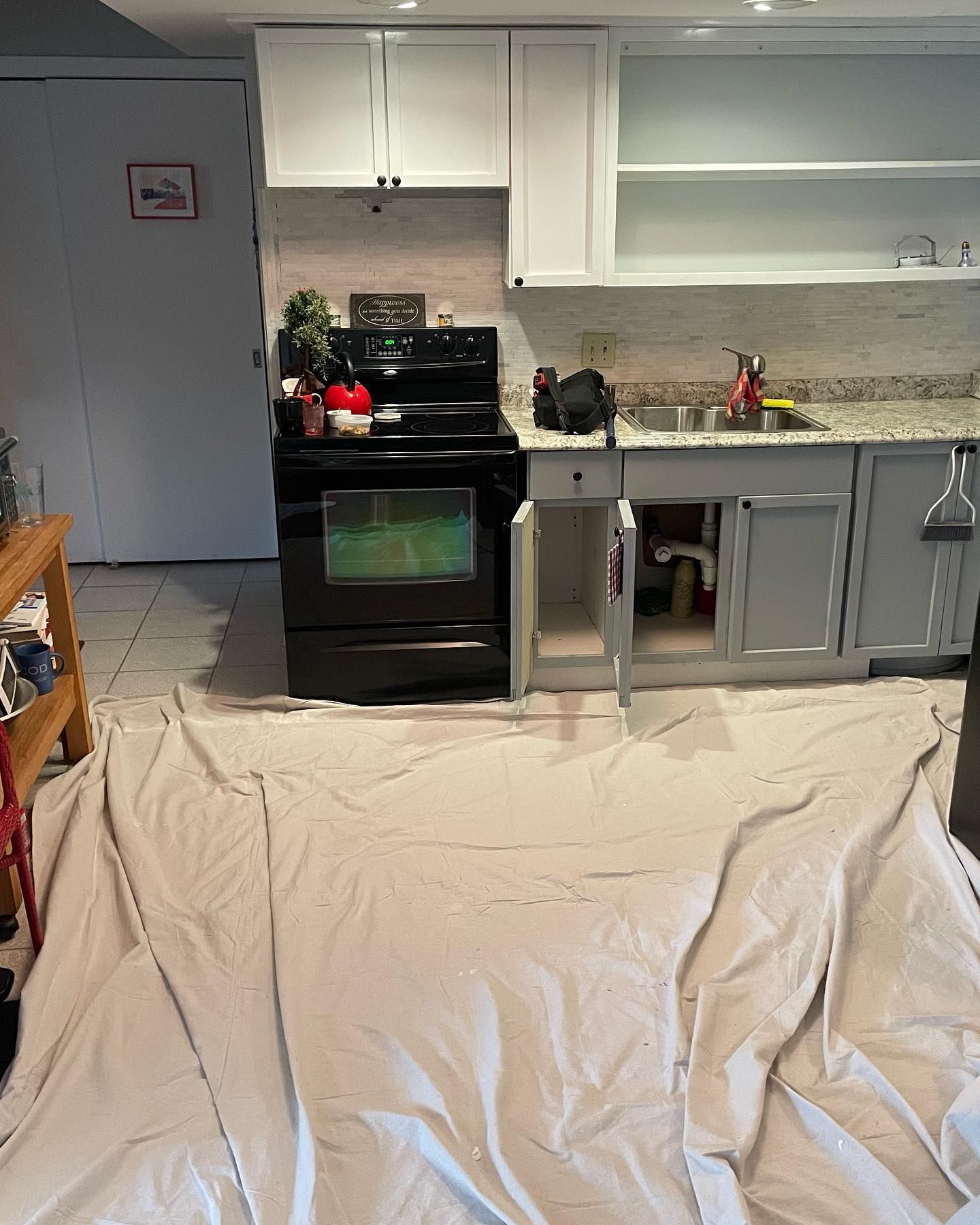 Kitchen with partially painted cabinets, stove, sink, and protective drop cloth on the floor.