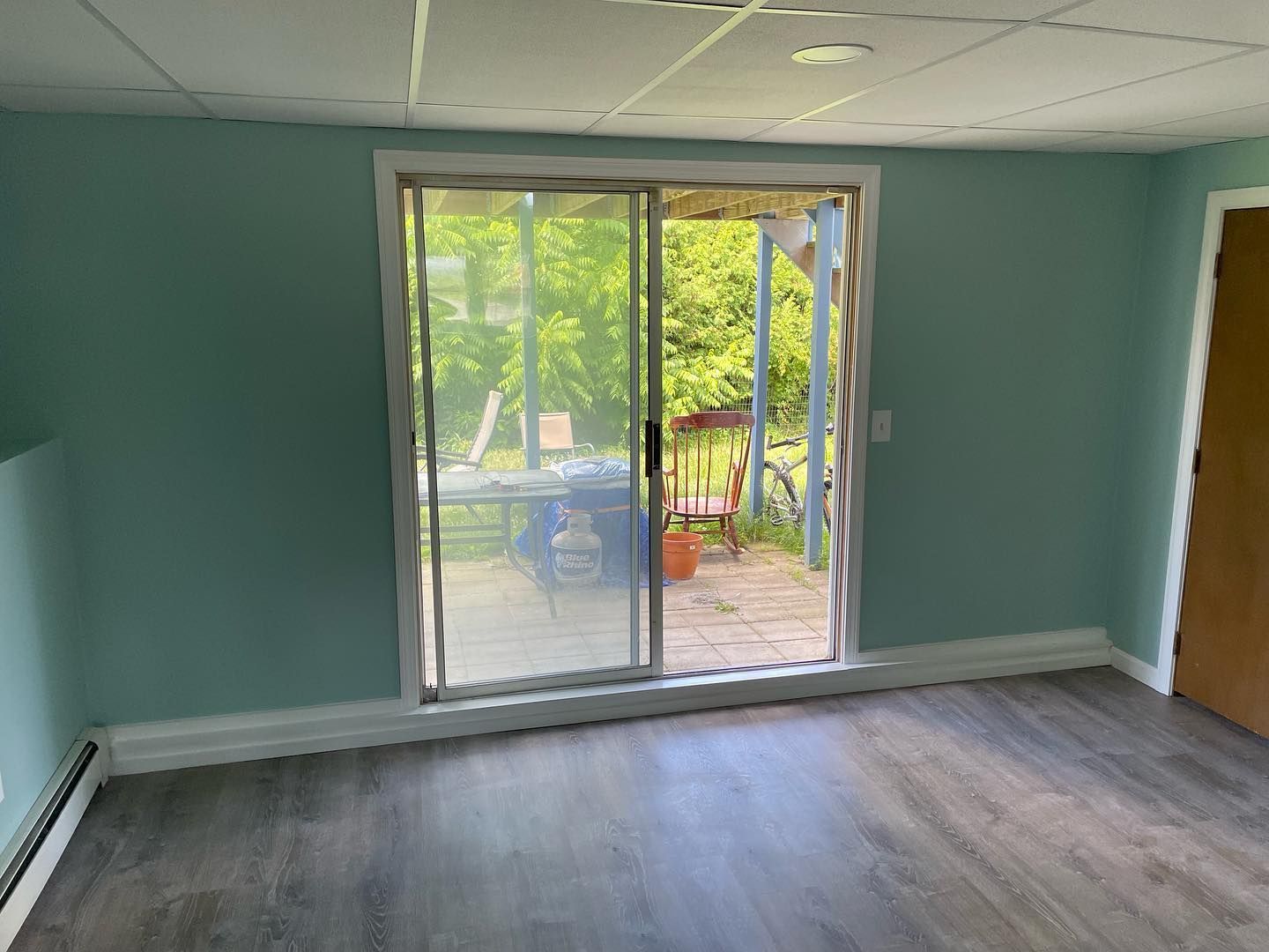 Room with sliding glass door open to an outdoor patio; teal walls, gray flooring, white trim.