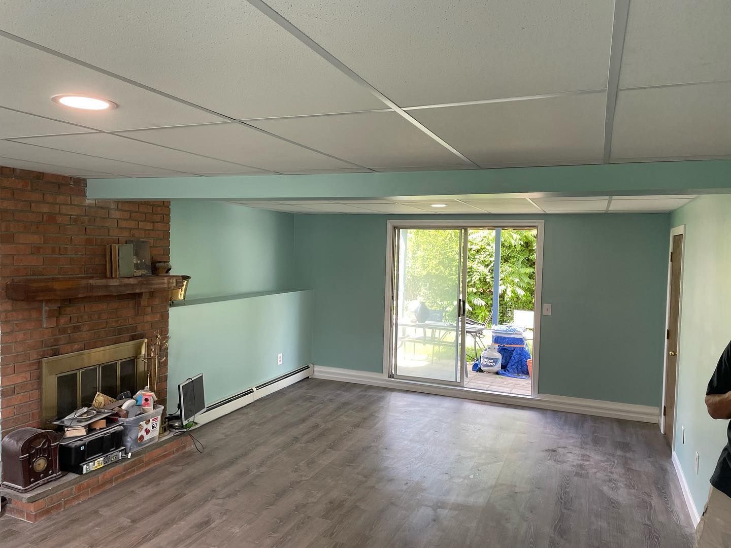 Room with a brick fireplace, sliding glass door, and pale green walls and ceiling. Wooden floors.