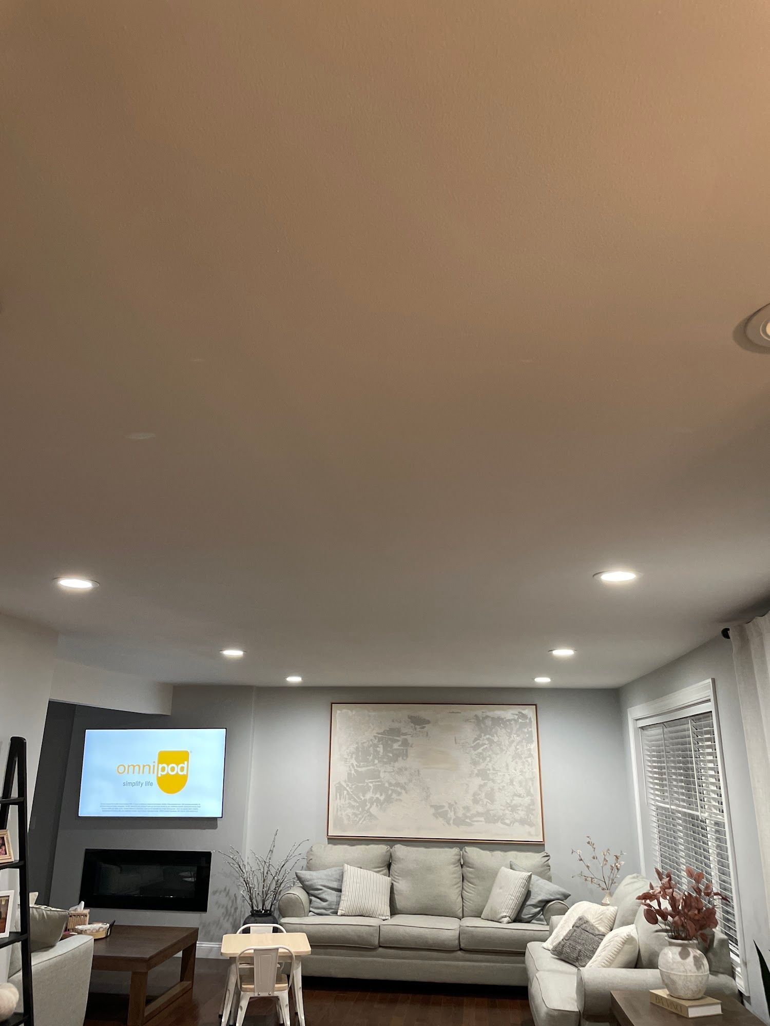 Living room with light gray walls, white couch, artwork, and TV above fireplace.