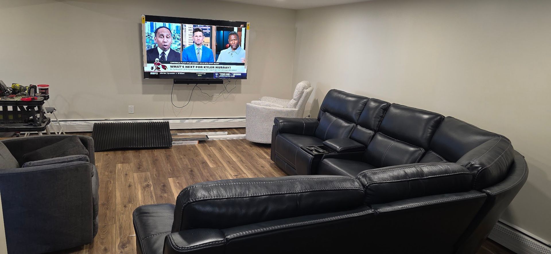 Living room with black leather sectional, TV on wall, and hardwood floors.