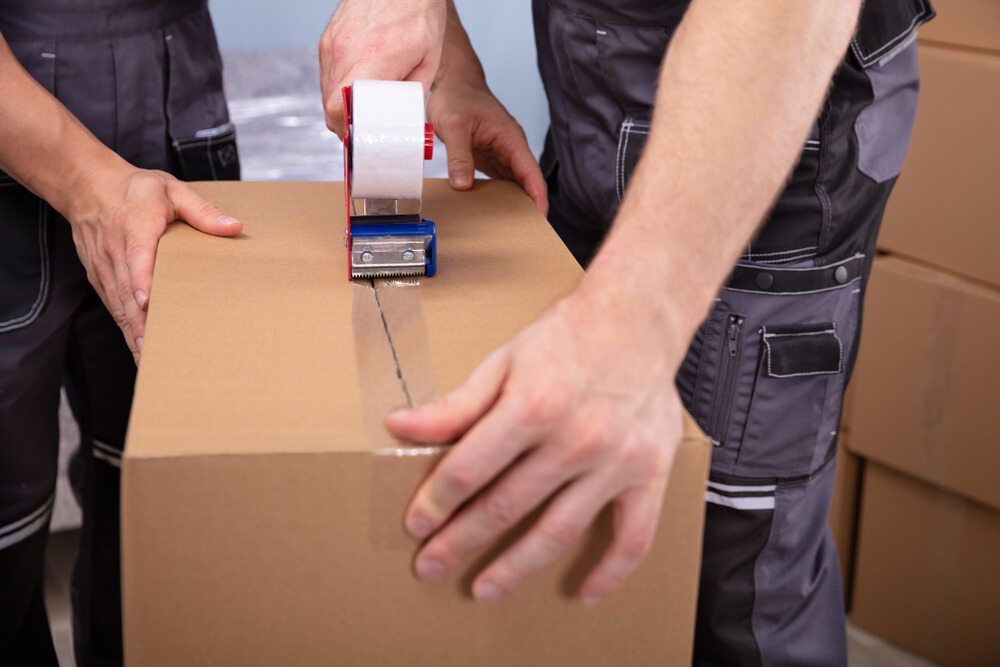 Two Men Are Taping a Cardboard Box With Tape — FNQ Furniture Removals in Mossman, QLD