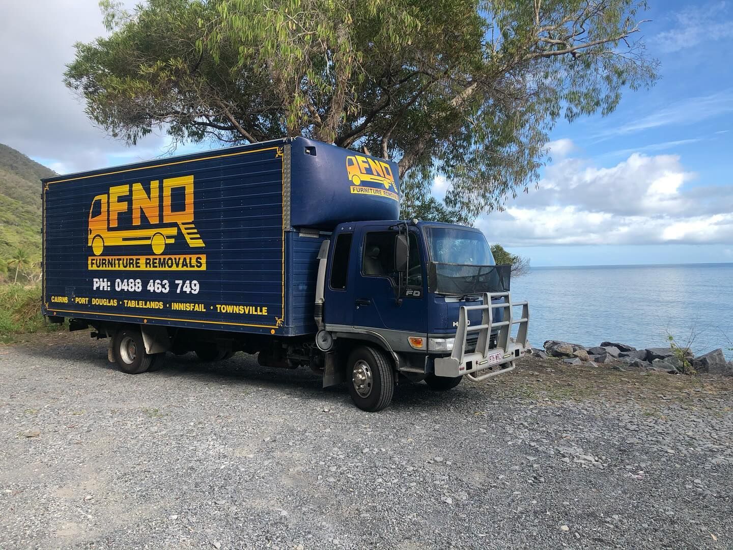 A Man is Carrying a Cardboard Box in Front of a Pile of Cardboard Boxes — FNQ Furniture Removals in Mossman, QLD