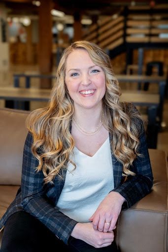 A woman is sitting at a table wearing a necklace and smiling.