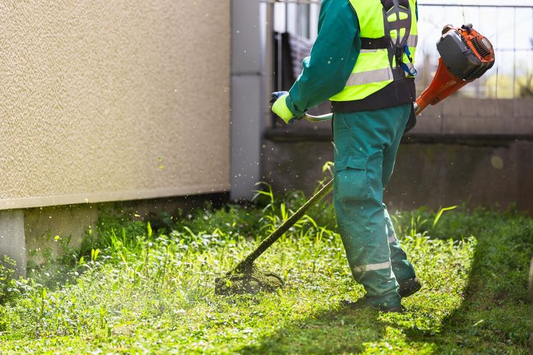 A man is using a lawn mower to cut grass in front of a building.