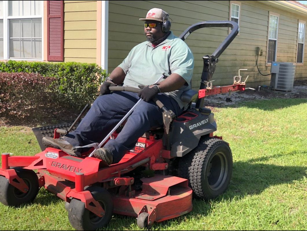 A man is riding a red lawn mower in front of a house.