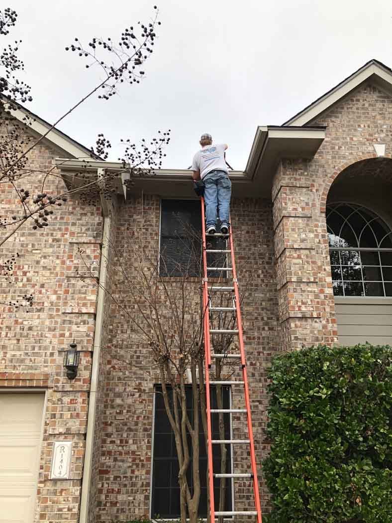 a man on a ladder cleaning the gutters of a brick house