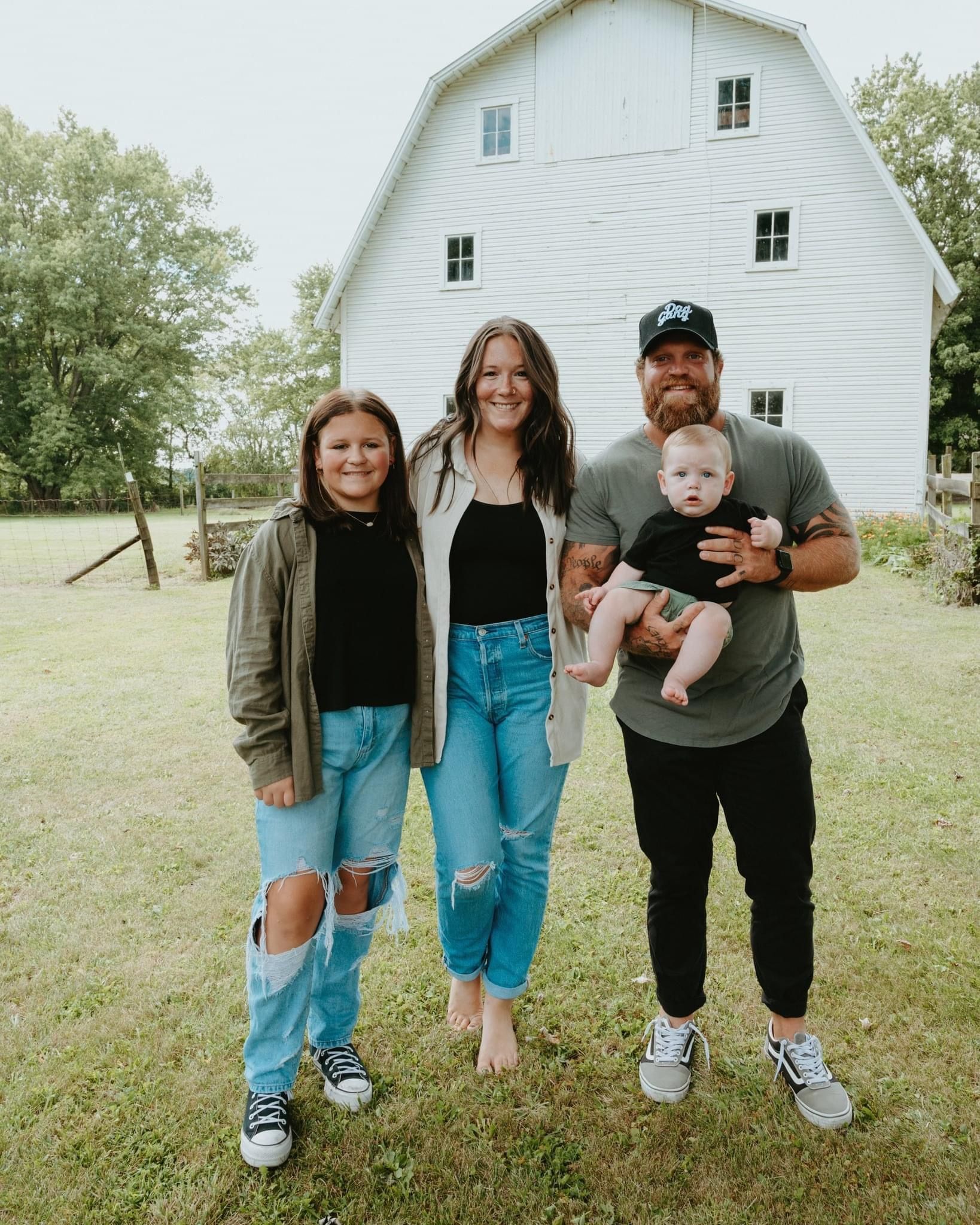 A family is posing for a picture in front of a white barn.