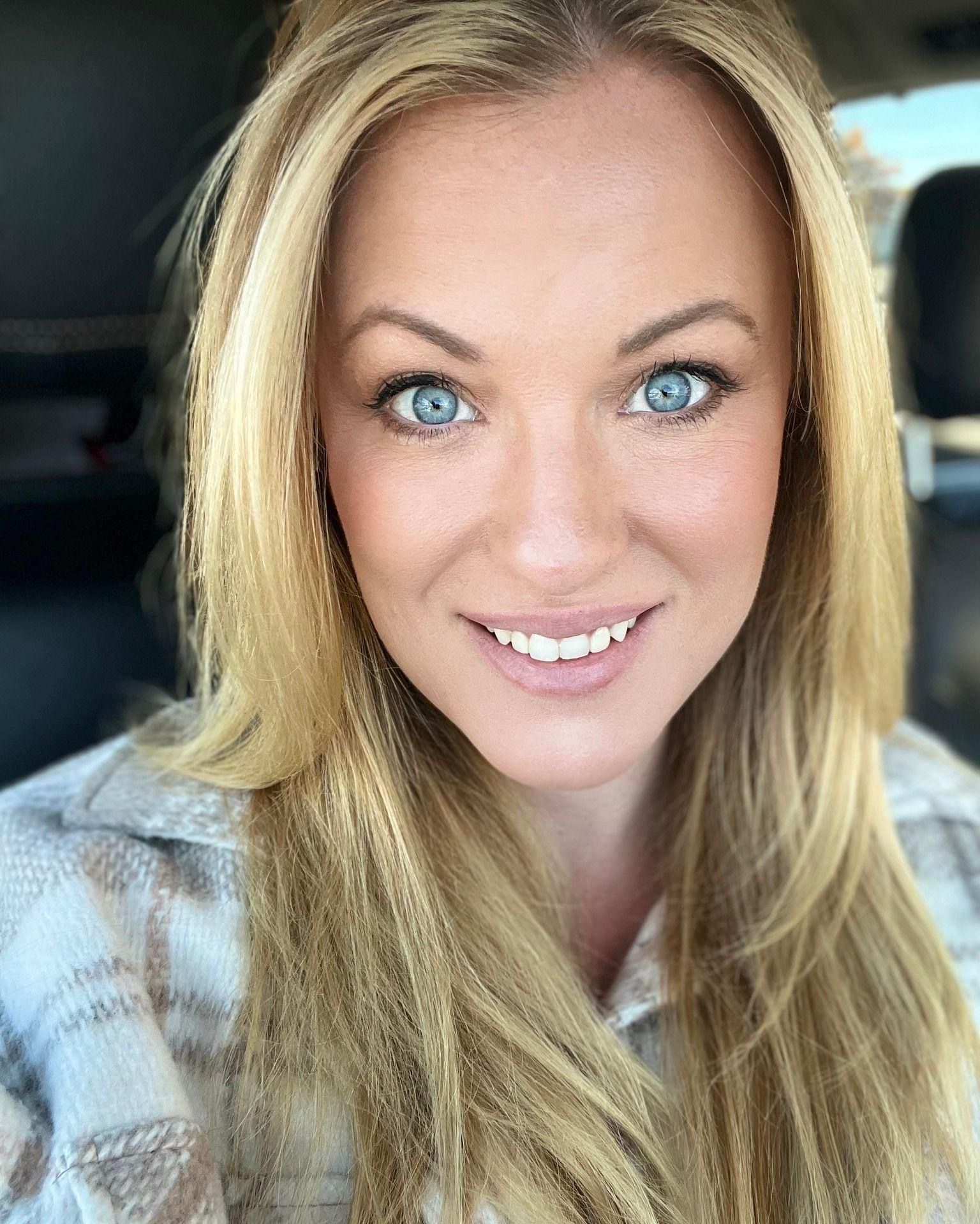 A woman with long blonde hair and blue eyes is smiling for the camera.