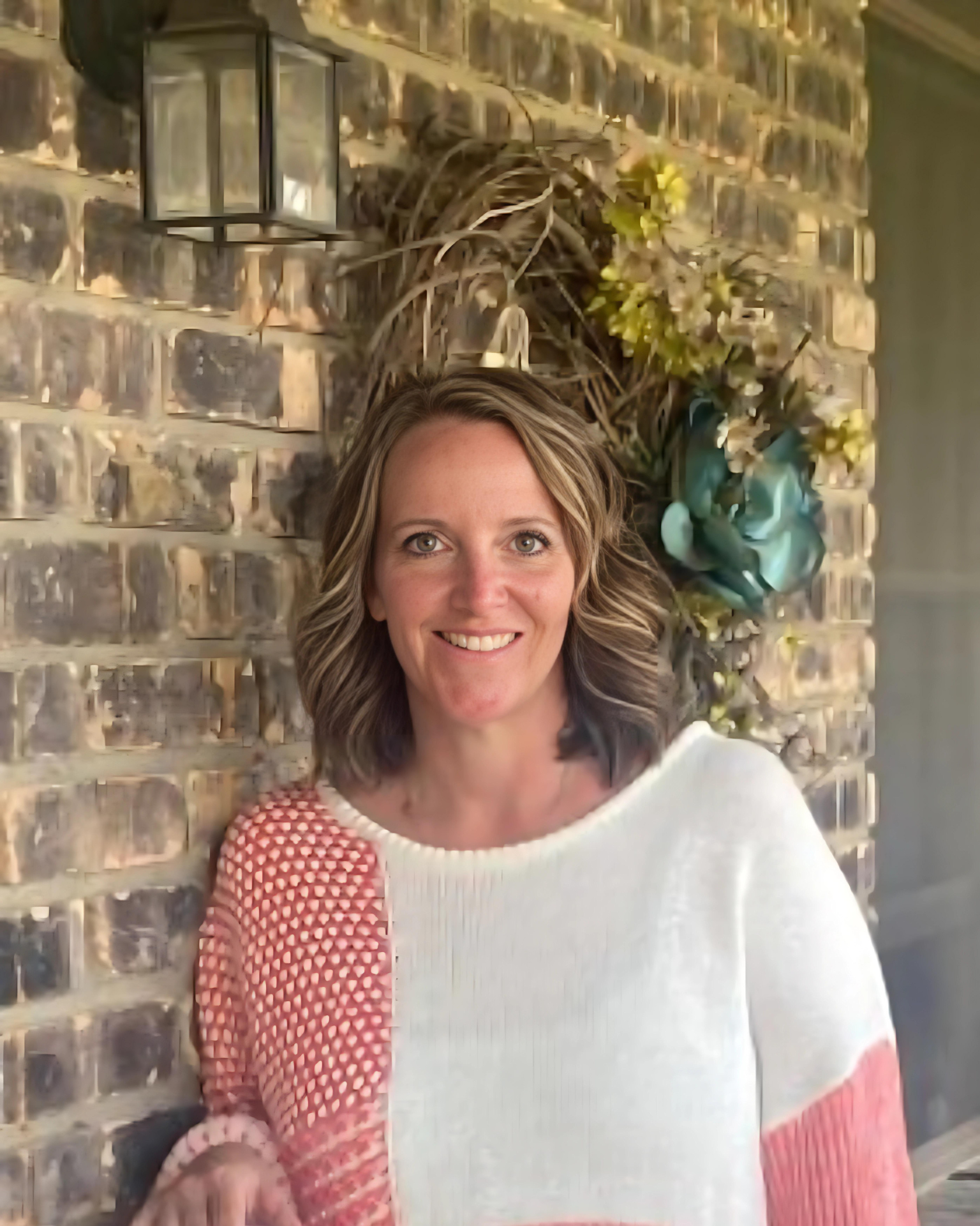 A woman in a pink and white sweater is standing in front of a brick wall.