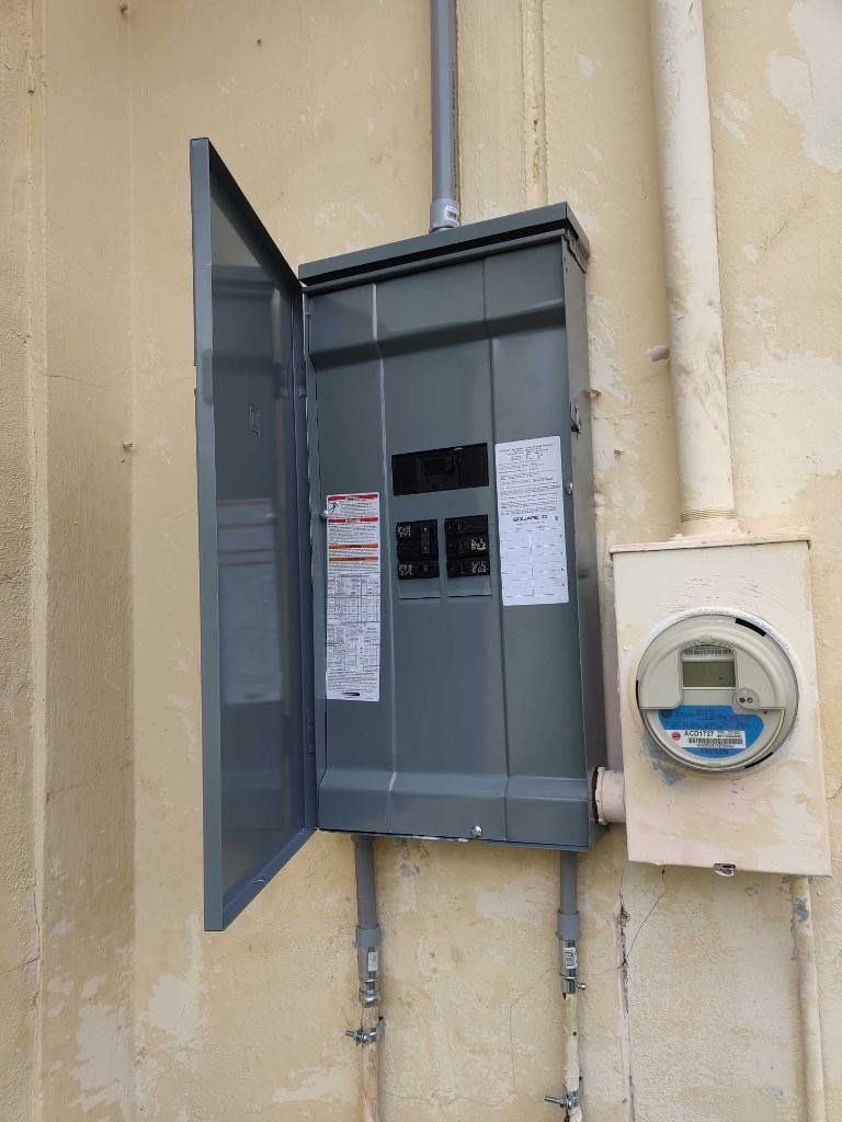 A electrical box is hanging on a wall next to a meter.