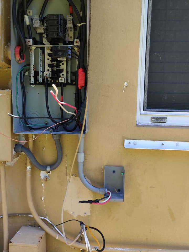 A box with wires coming out of it is on a wall next to a window.