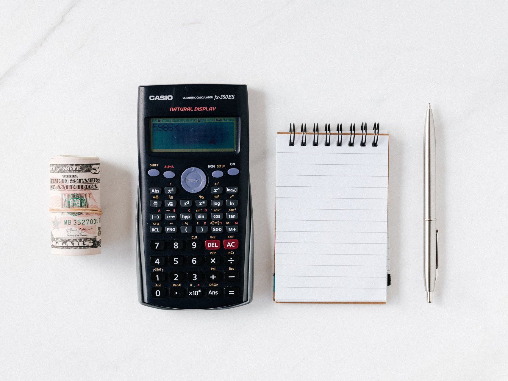 photo of items on desk: money, calculator, notepad, pen