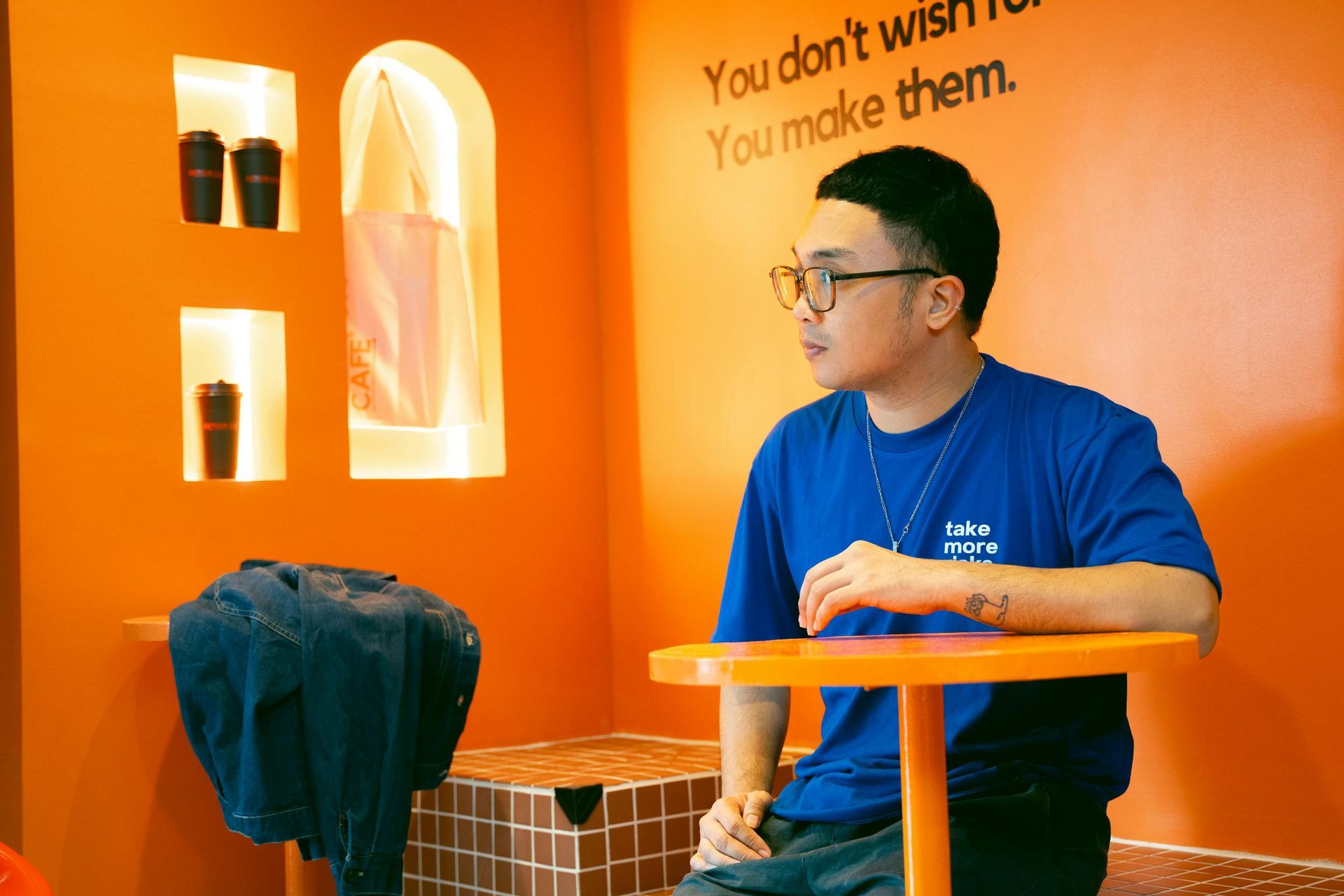 A man is sitting at a table in front of an orange wall.