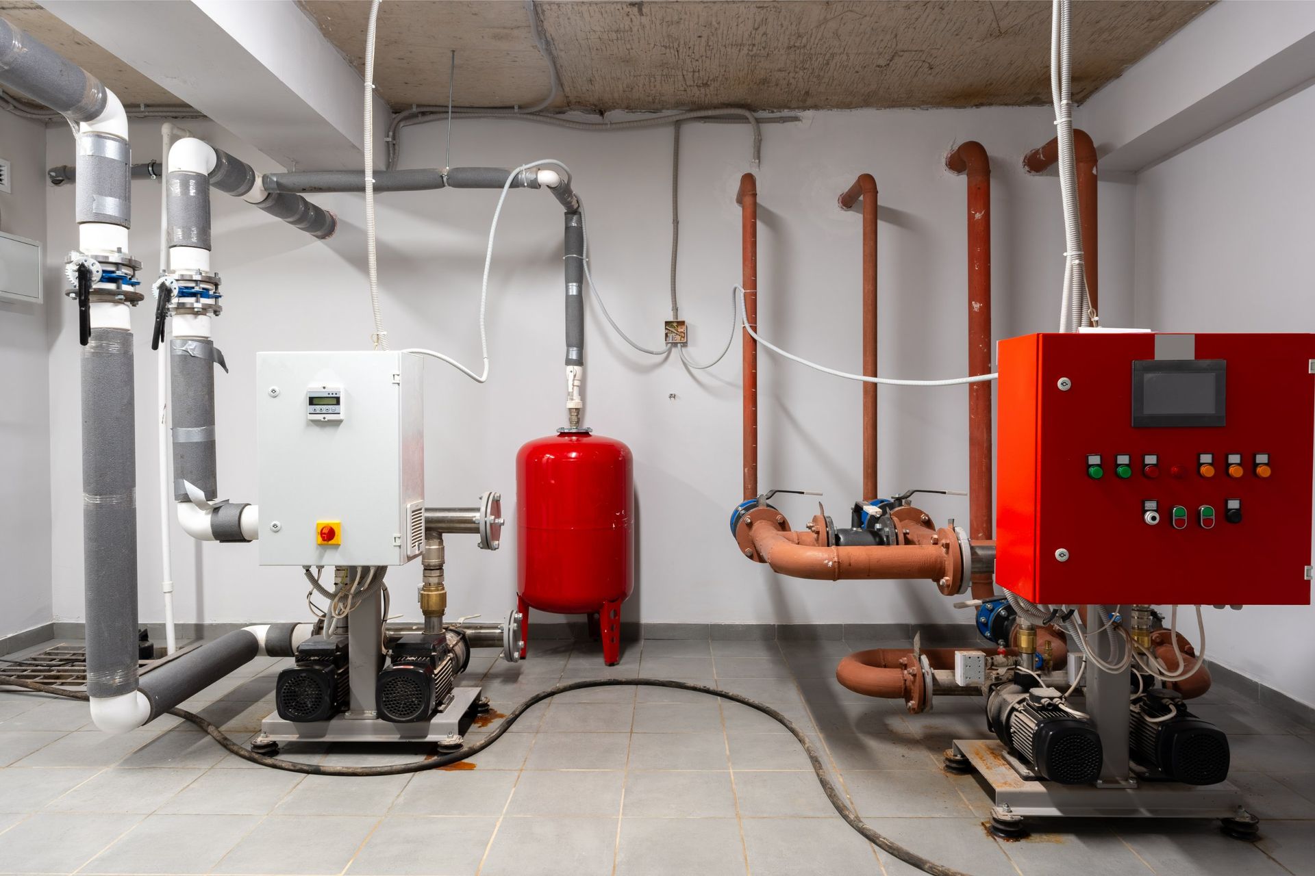 Equipment room with pipes, pumps, and control panels in white and red.