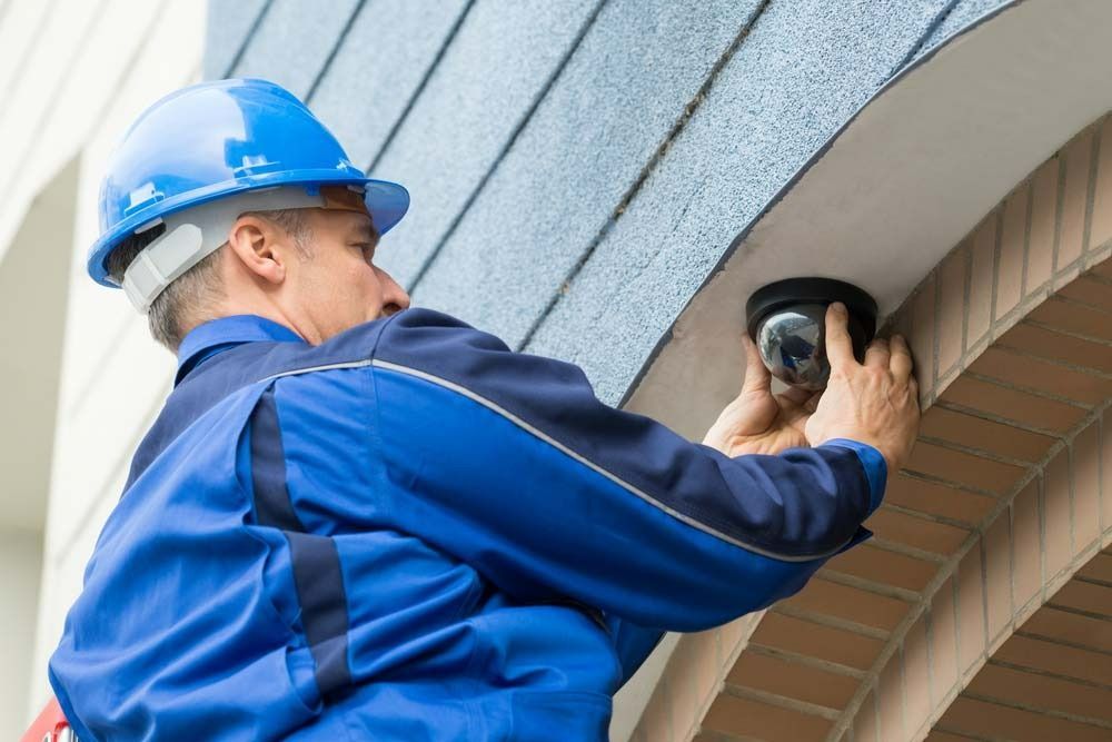 A Man Is Installing A Security Camera On The Side Of A Building — On Guard Security & Communications In Wallsend, NSW