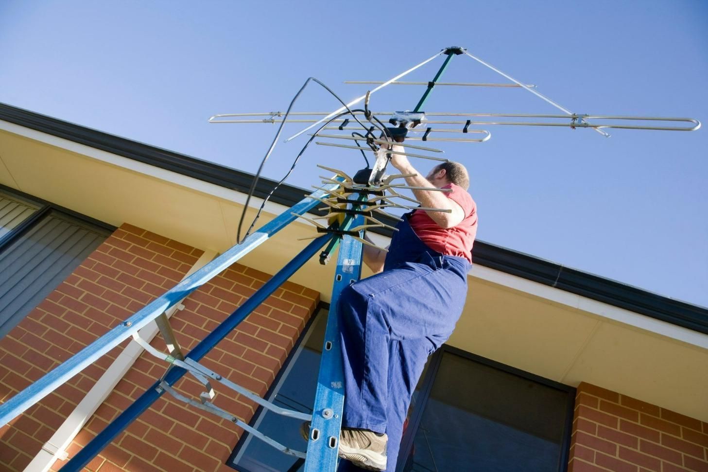 A Man Is Sitting On A Ladder Working On An Antenna — On Guard Security & Communications In Wallsend, NSW